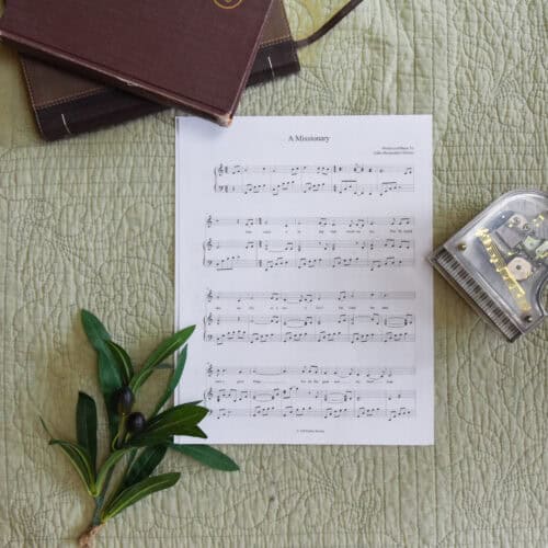 Sheet music to "A Missionary". The music is surrounded by a model piano, a bible, and a small leafy plant.