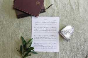 Sheet music to "America". The music is surrounded by a model piano, a bible, and a small leafy plant.