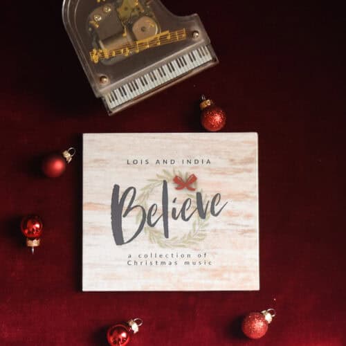 CD of "Believe: A Collection of Christmas Music". The music is surrounded by a model piano, a bible, and a small leafy plant.