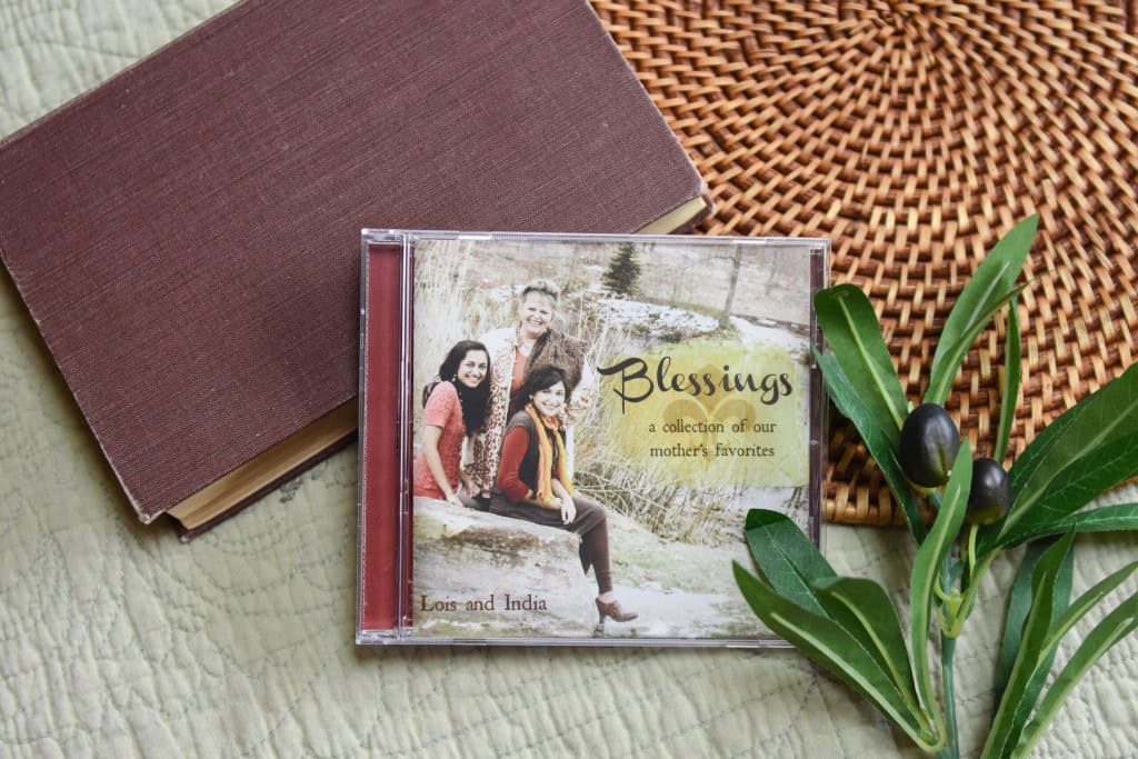 CD of "Blessings: A Collection of Our Mother's Favorites". The music is surrounded by a bible and a small leafy plant.