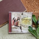 CD of "Blessings: A Collection of Our Mother's Favorites". The music is surrounded by a bible and a small leafy plant.