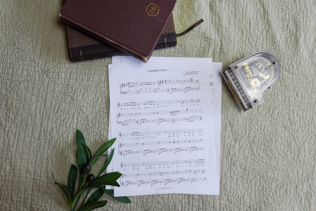 Sheet music to "Consider Christ". The music is surrounded by a model piano, a bible, and a small leafy plant.