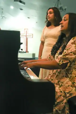 Lois and India singing at a church. Lois is on the piano and there is a cross in the background
