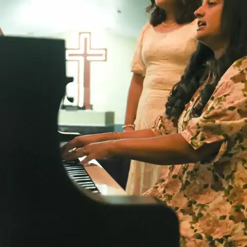 Lois and India singing at a church. Lois is on the piano and there is a cross in the background