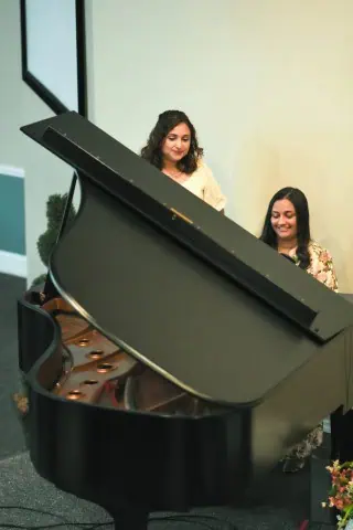 Lois and India at the piano. The piano is in the foreground and you can see them behind it.