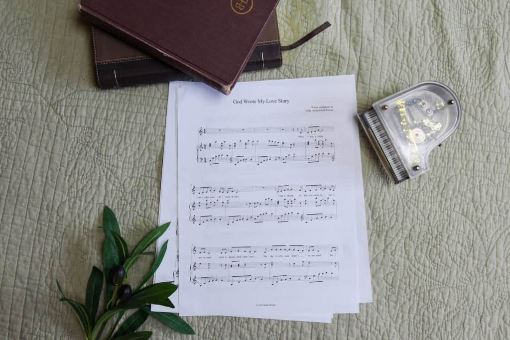 Sheet music to "God Wrote My Love Story". The music is surrounded by a model piano, a bible, and a small leafy plant.
