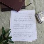 Sheet music to "God Wrote My Love Story". The music is surrounded by a model piano, a bible, and a small leafy plant.