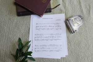 Sheet music to "God Wrote My Love Story". The music is surrounded by a model piano, a bible, and a small leafy plant.