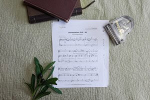 Sheet music to "Lamentations 3:15-26". The music is surrounded by a model piano, a bible, and a small leafy plant.