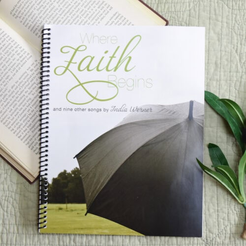 Sheet music book "Where Faith Begins" laying on an open bible with a green plant beside it.