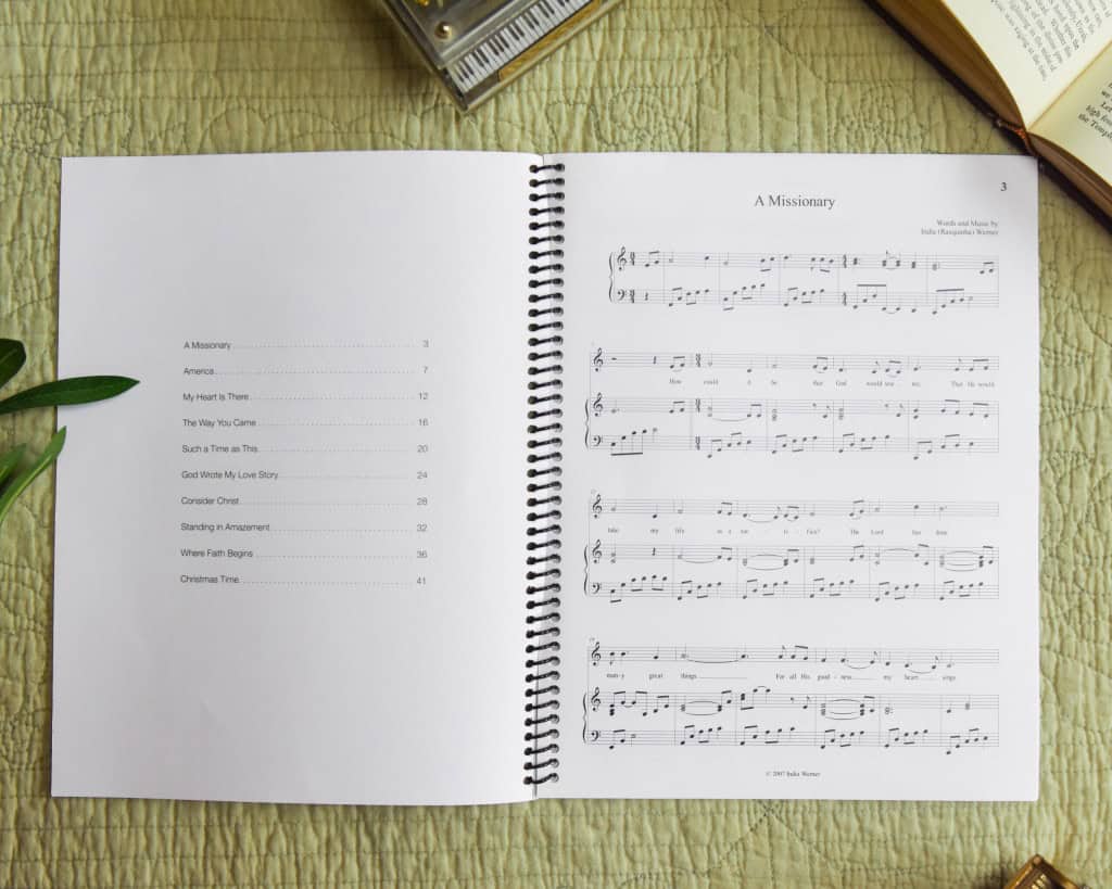 Sheet music book "Where Faith Begins" laying open with table of contents showing. On the table is a bible, model piano, and a green plant.