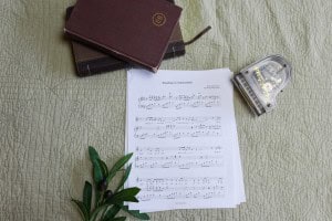 Sheet music to "Standing in Amazement". The music is surrounded by a model piano, a bible, and a small leafy plant.