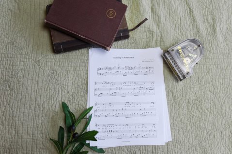 Sheet music to "Standing in Amazement". The music is surrounded by a model piano, a bible, and a small leafy plant.