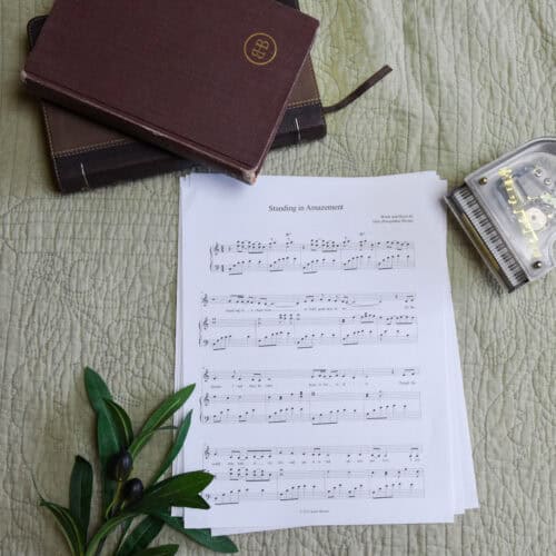 Sheet music to "Standing in Amazement". The music is surrounded by a model piano, a bible, and a small leafy plant.