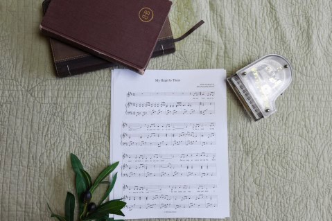 Sheet music to "My Heart is There". The music is surrounded by a model piano, a bible, and a small leafy plant.