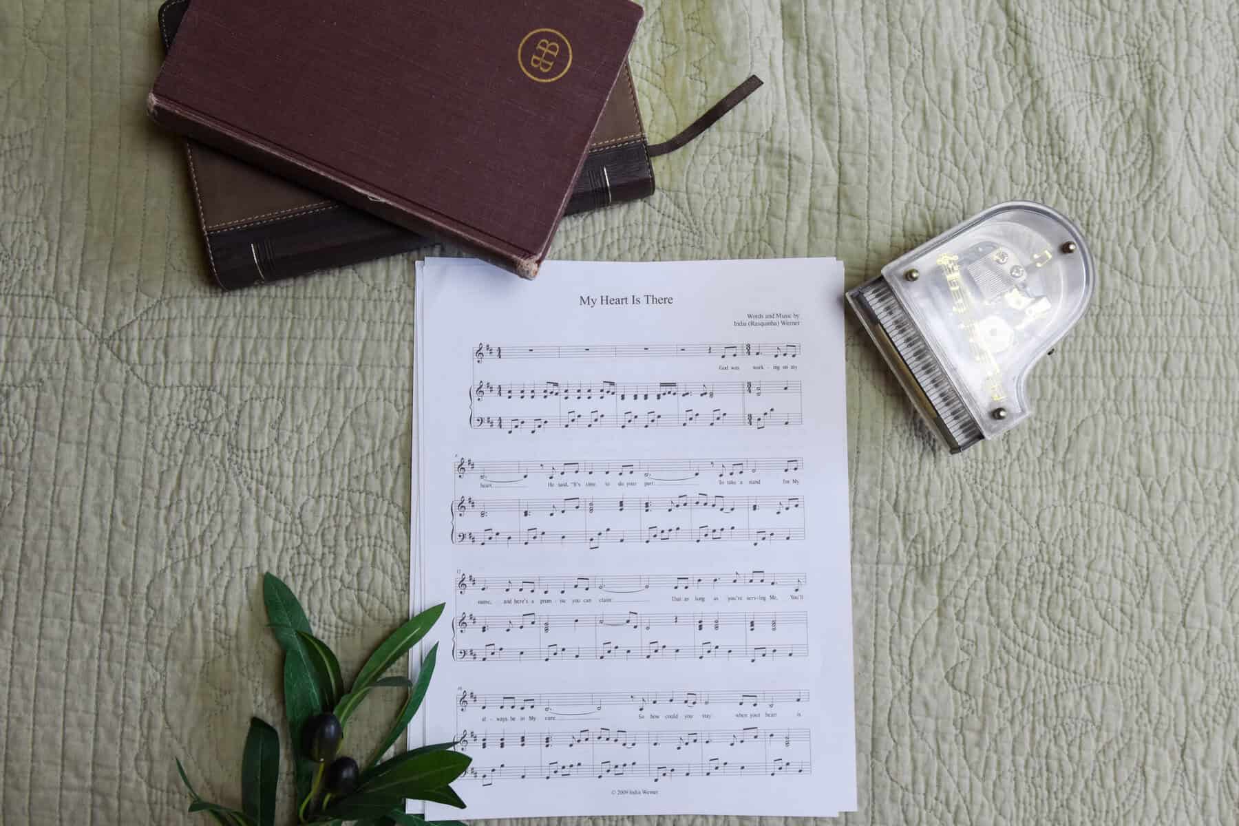 Sheet music to "My Heart is There". The music is surrounded by a model piano, a bible, and a small leafy plant.