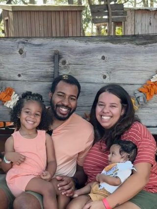 the Simon family. There is a Man, Woman, and two children smiling in front of a wooden backdrop.