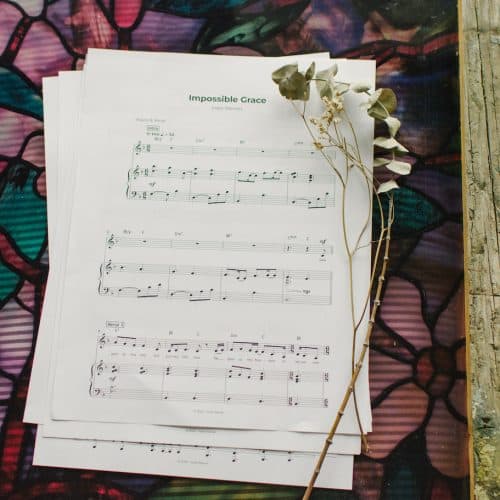 Sheet music to "Impossible Grace" laying on a table surrounded by floral arrangements