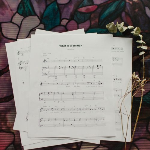 The Sheet music to "What is Worship" splayed out of a table with floral arrangements around it.